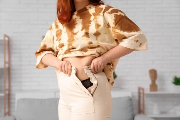 Image of woman trying to do her trousers up after pregnancy weight gain Beccles